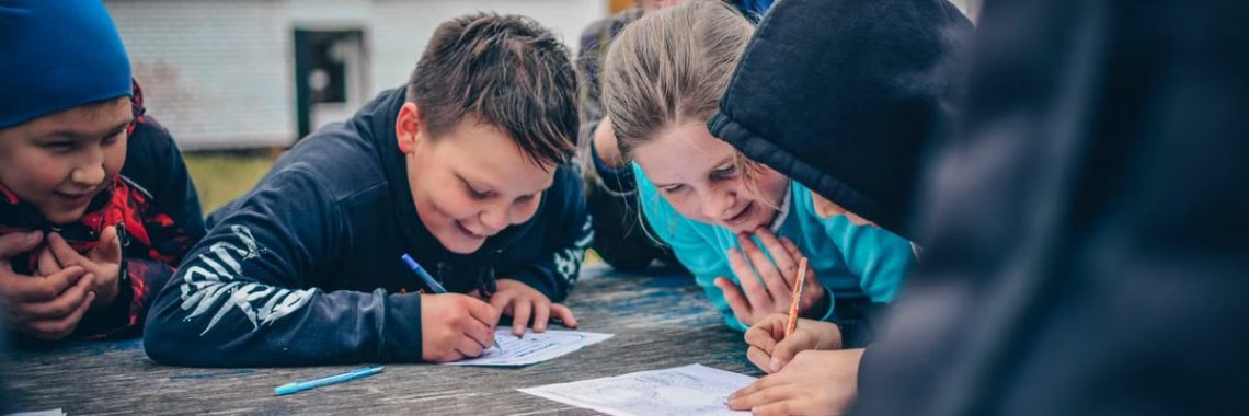 Happy children drawing together outdoors on a wooden table, fostering creativity and teamwork.